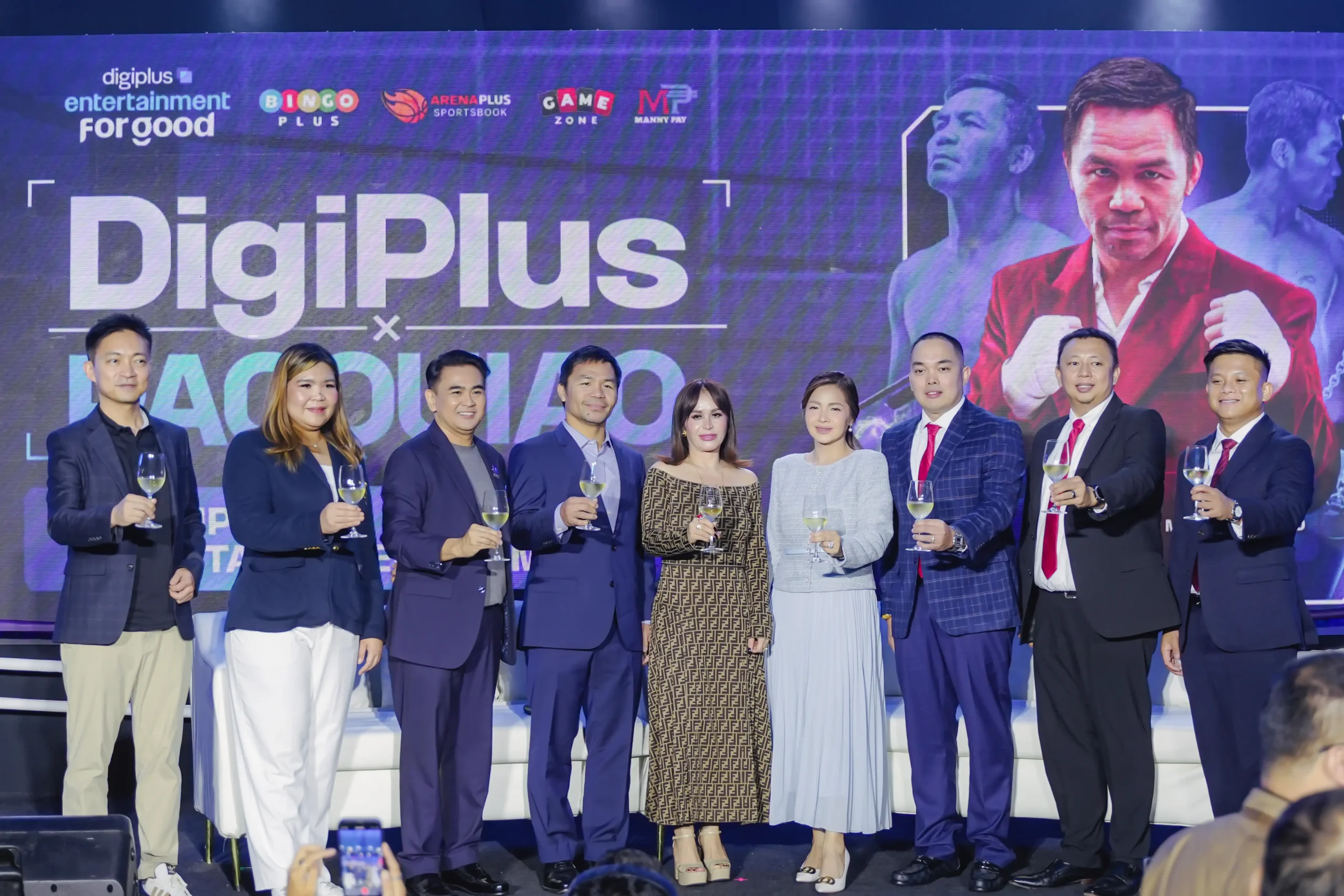 Group of ten professionals toasting with wine glasses on stage in front of a large Digiplus banner.
