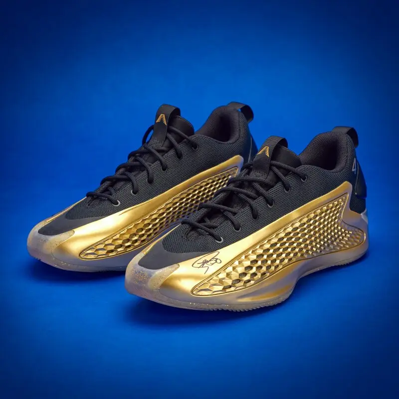 Pair of black and gold athletic sneakers with honeycomb-patterned side panels on a blue backdrop