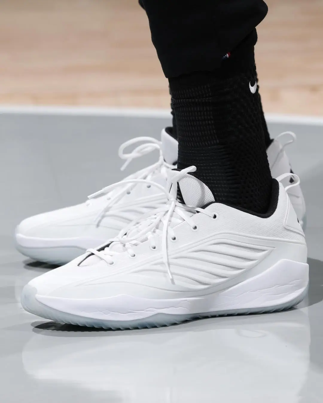 White athletic sneakers with wavy side panels worn with black socks on a glossy floor, close-up side view.