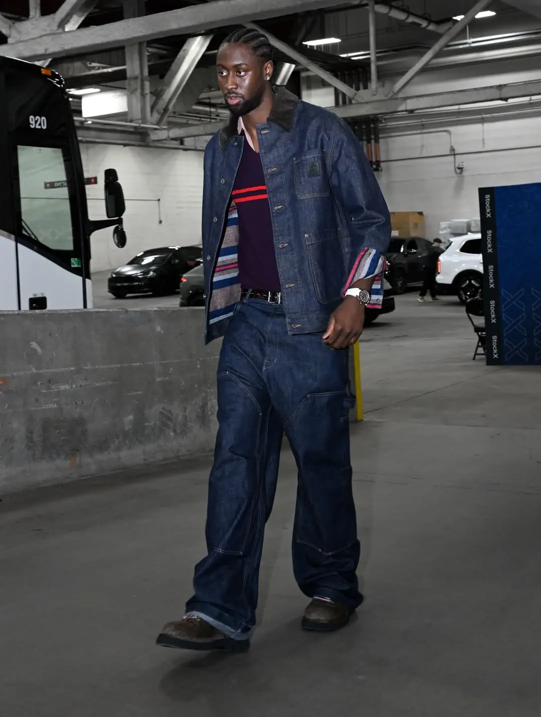 Man in a dark denim jacket and oversized jeans walking through an indoor parking garage.