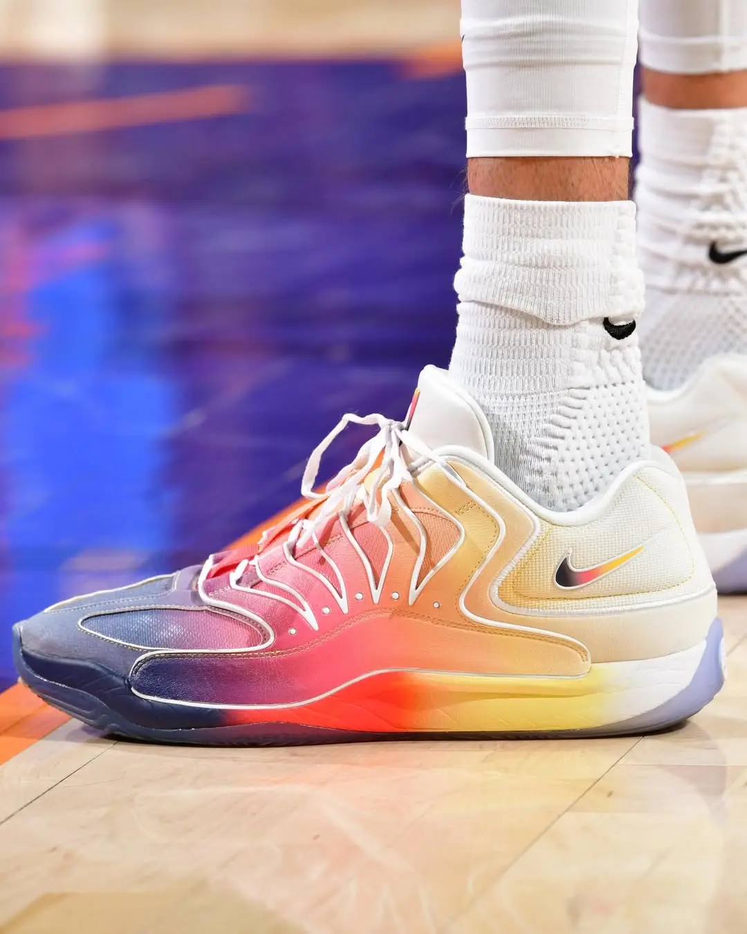Bright gradient basketball sneaker with white laces and socks on a wooden court, Nike logo visible on the side.