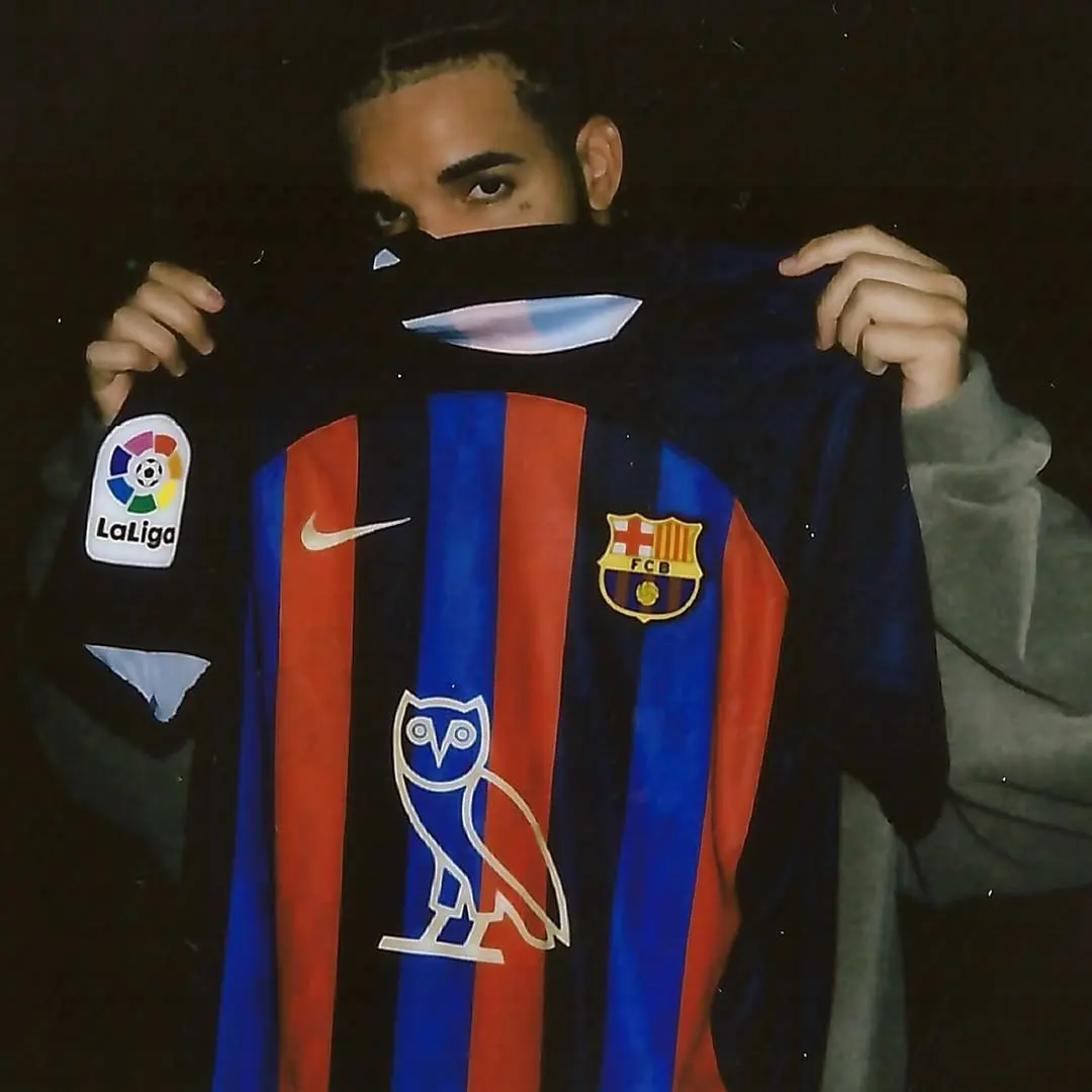 Person holding up a FC Barcelona jersey with a La Liga patch on the sleeve against a dark background.