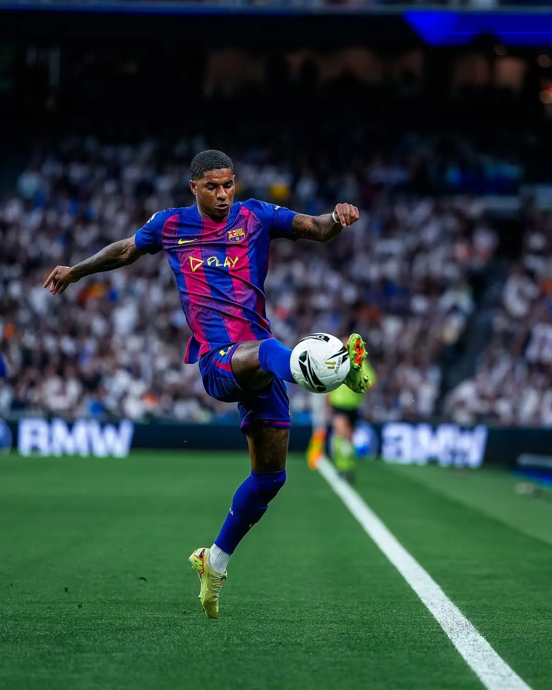 Soccer player in blue and red FC Barcelona kit kicking the ball along the touchline during a match with a crowded stadium in the background.