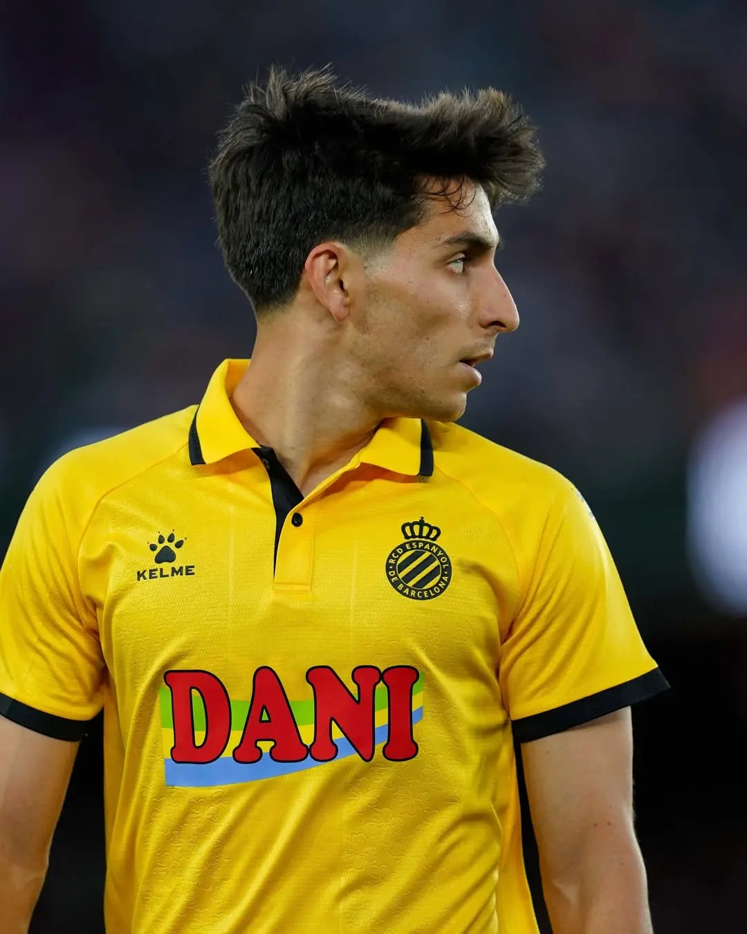 Soccer player in a bright yellow jersey seen in profile against a dark stadium background.