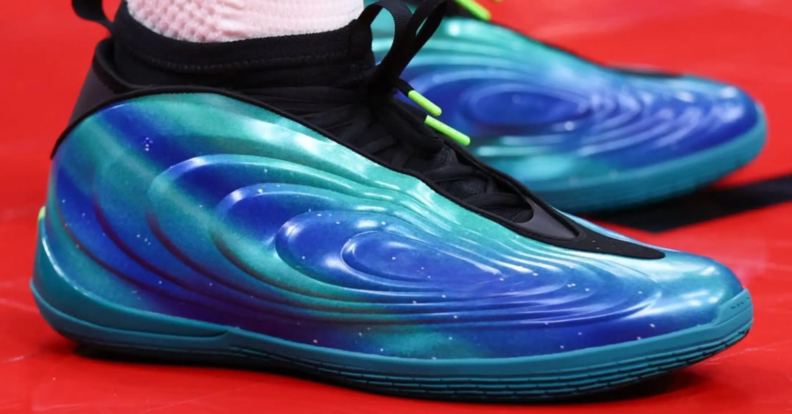 Close-up of a vibrant, multicolor athletic shoe with blue–green gradients and black laces on a red surface