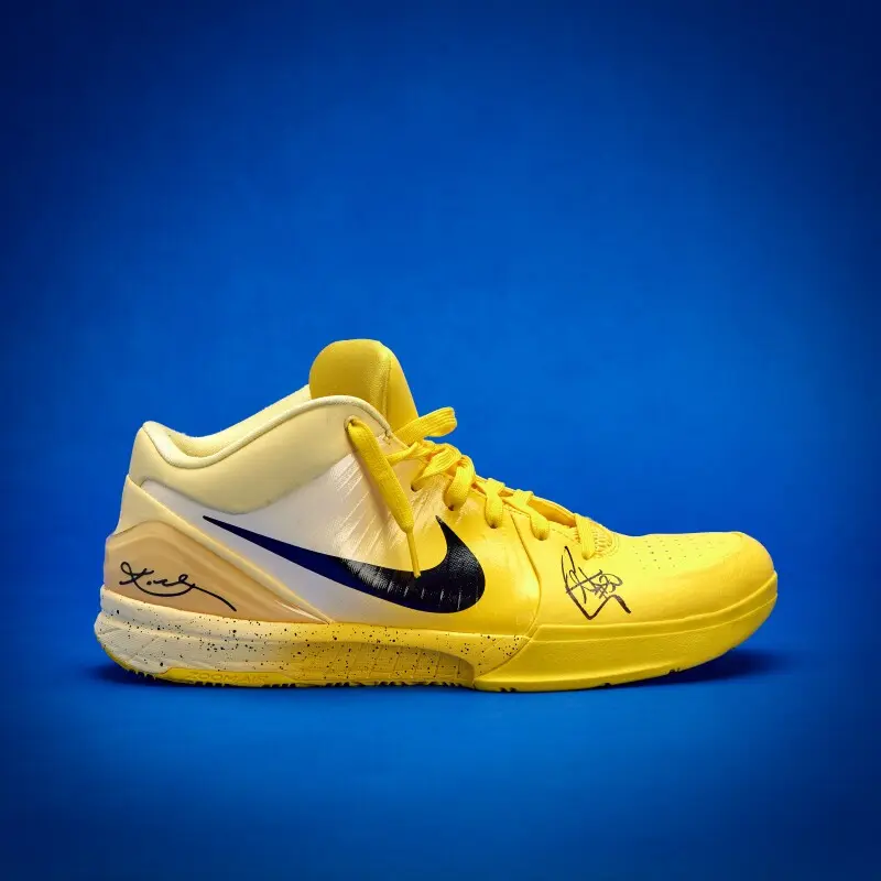 Yellow Nike basketball shoe on blue background, with black swoosh and autographs on the sides.