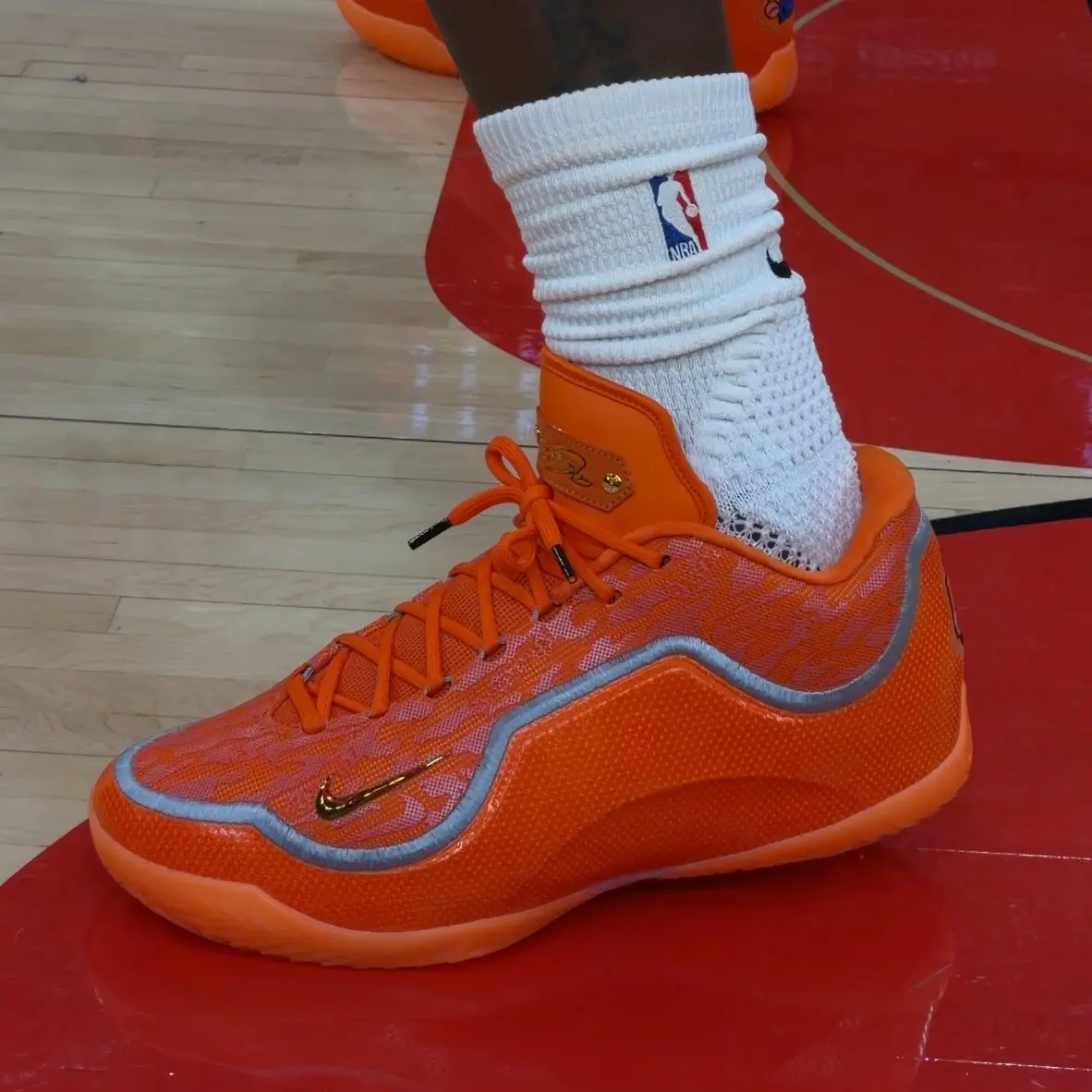 Orange basketball shoe with white knit sock on a wooden court floor, vibrant and detailed.
