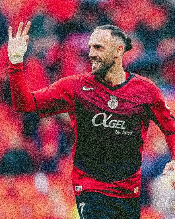 Soccer player with a short beard in a red and black kit waving to the crowd during a match.