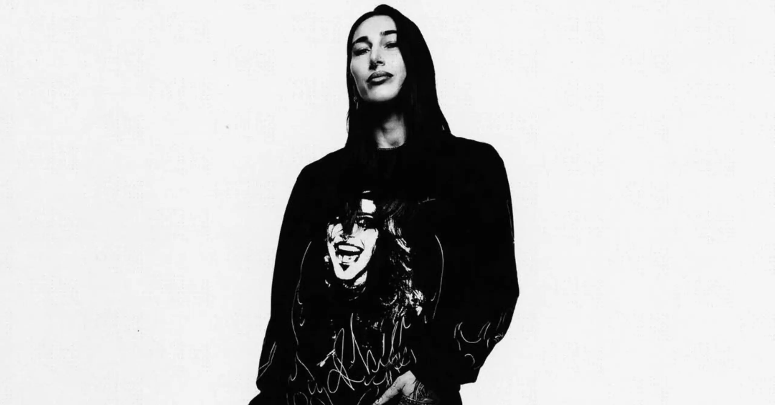 Person in a black hoodie with a graphic print on the shirt, standing against a light background (black-and-white photo).