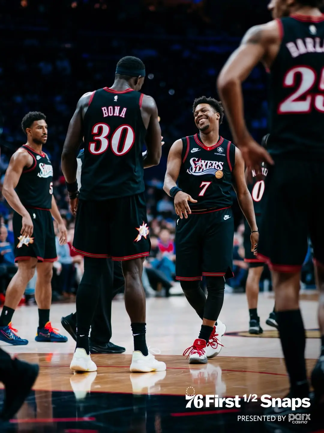 Saveclipapp_647286483_18577222030017054_3210848999622845758_n - the game Philadelphia 76ers players in black jerseys with red trim share a light moment on the court, high-fiving and smiling amid teammates and fans in the background.