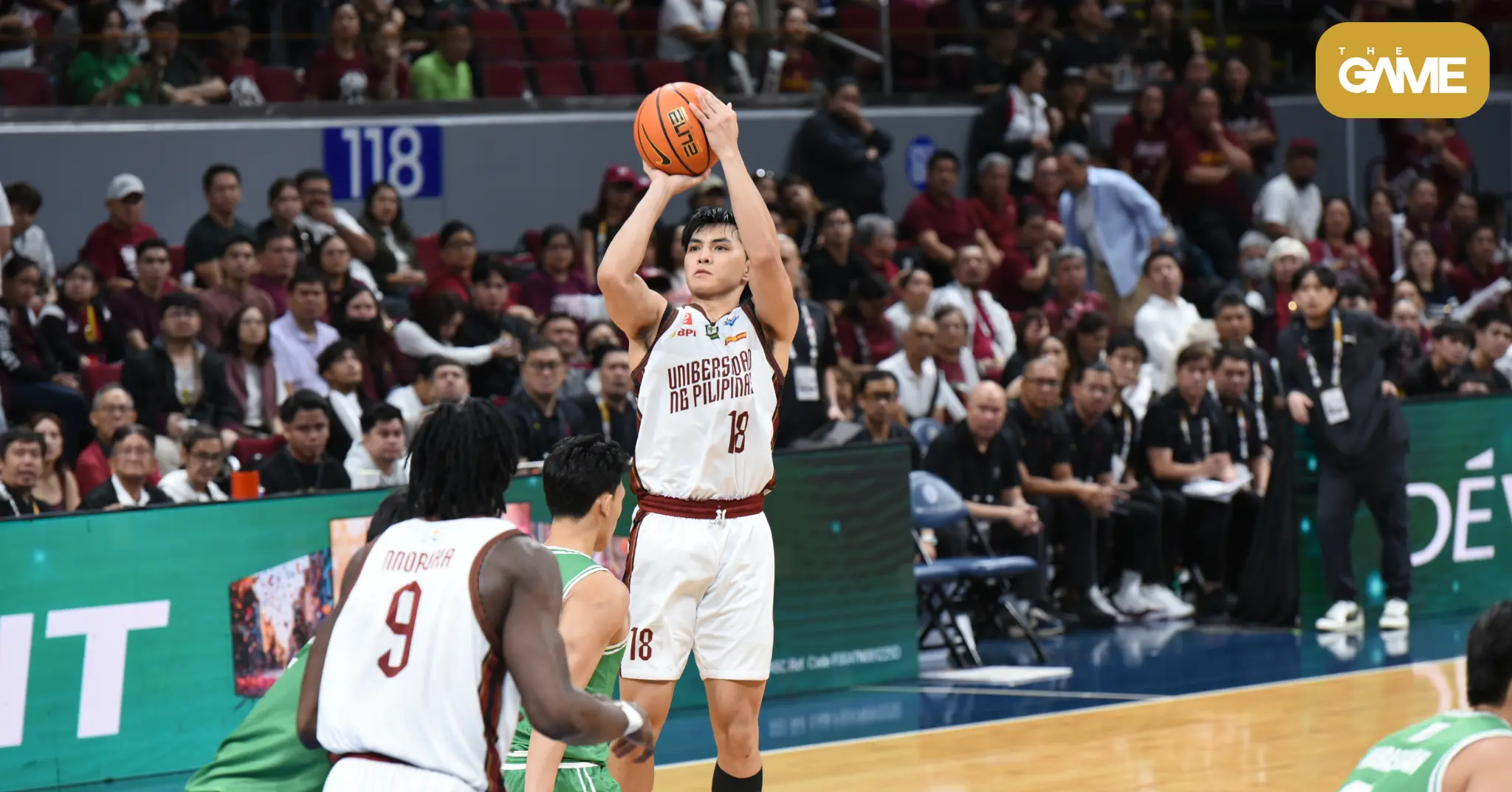 White-uniform basketball player (number 18) jumps to shoot the ball over defenders as a crowded arena watches the play likely during a college game in progress.