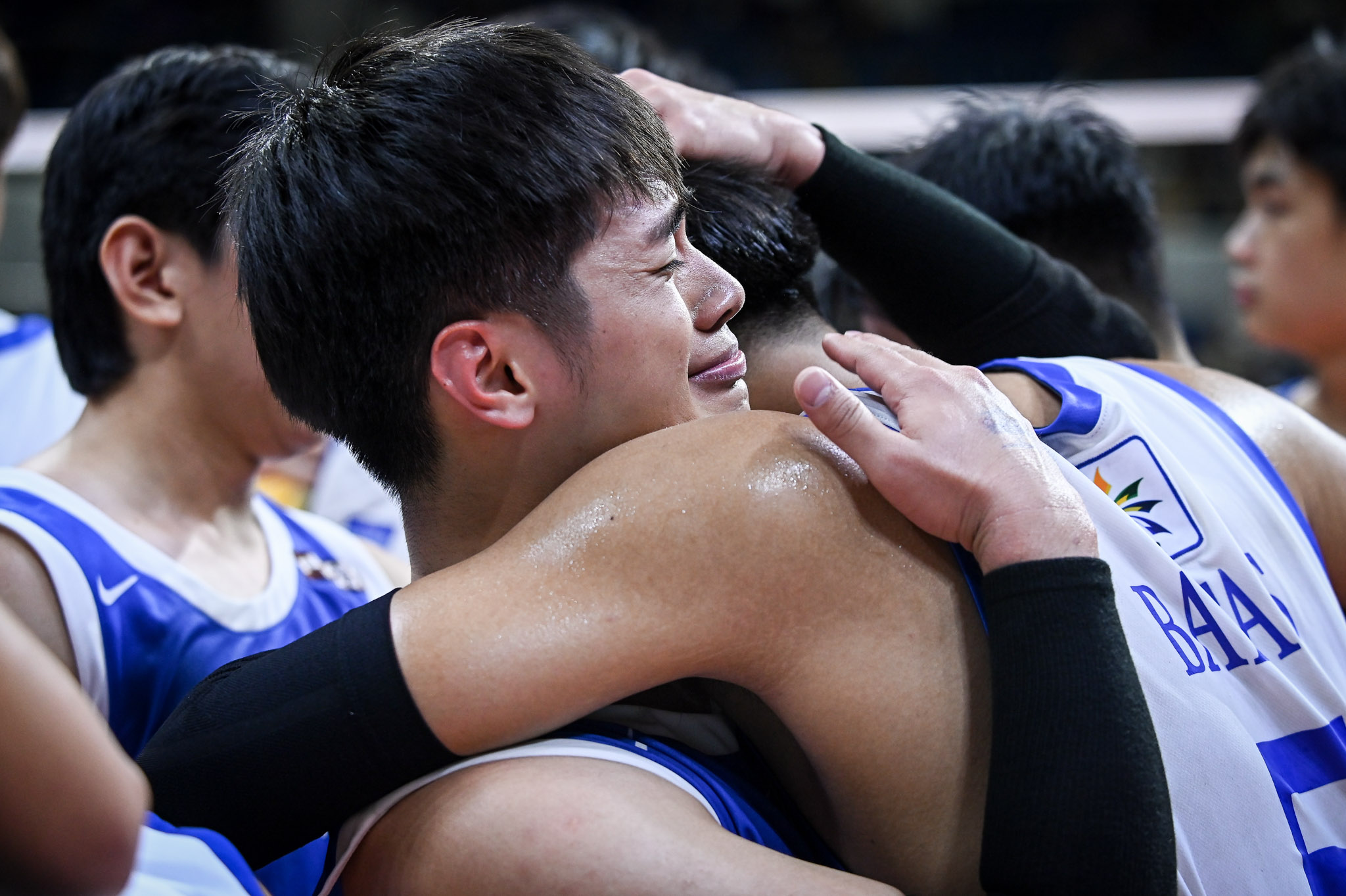 Uaap 88 mvb f4 admu vs feu- lance decastro - the game Two athletes in blue-and-white uniforms embrace in a group hug, celebrating after a game on the court.”,
