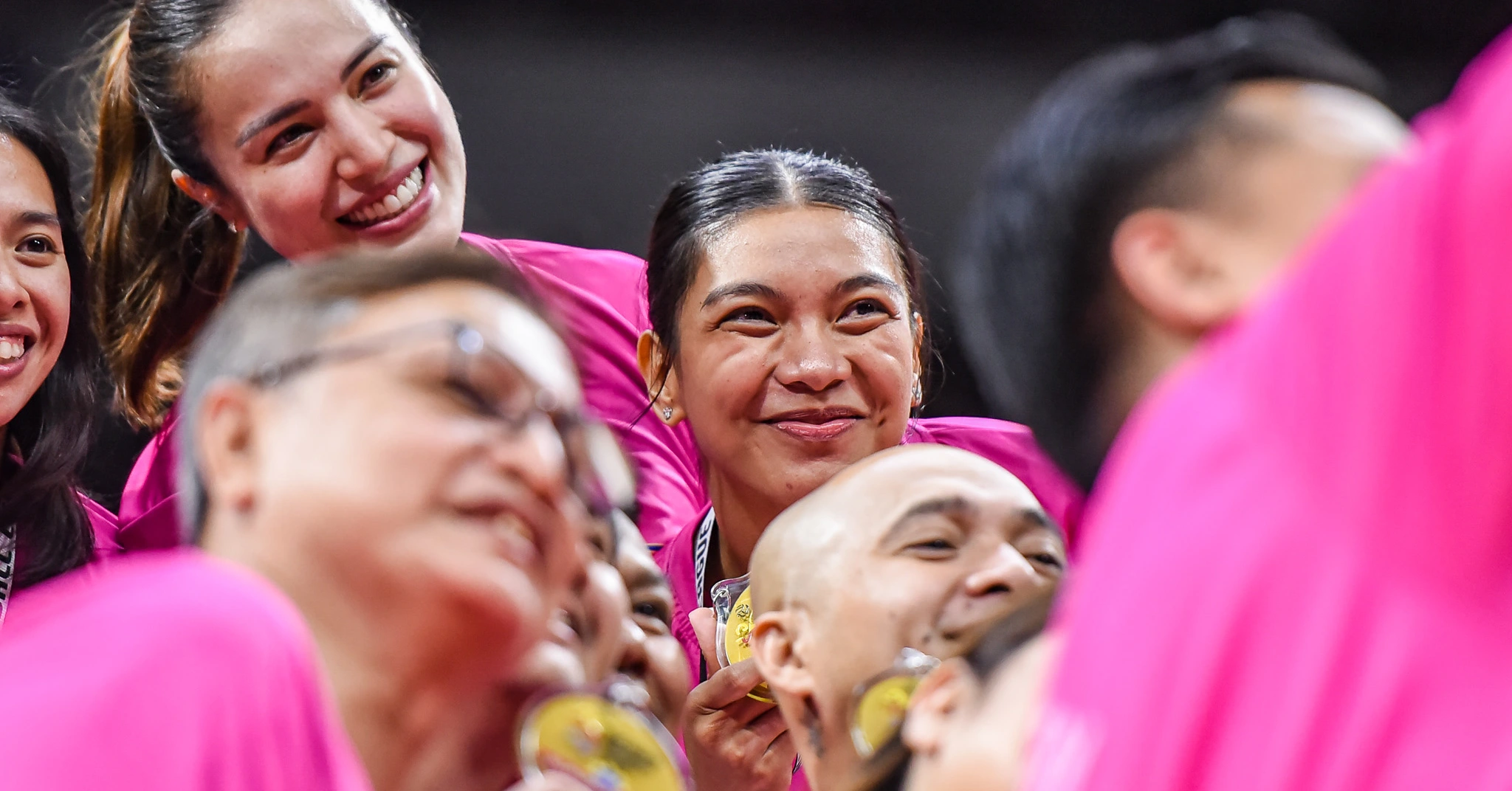Group of smiling people wearing bright pink shirts, close together at a celebratory event.