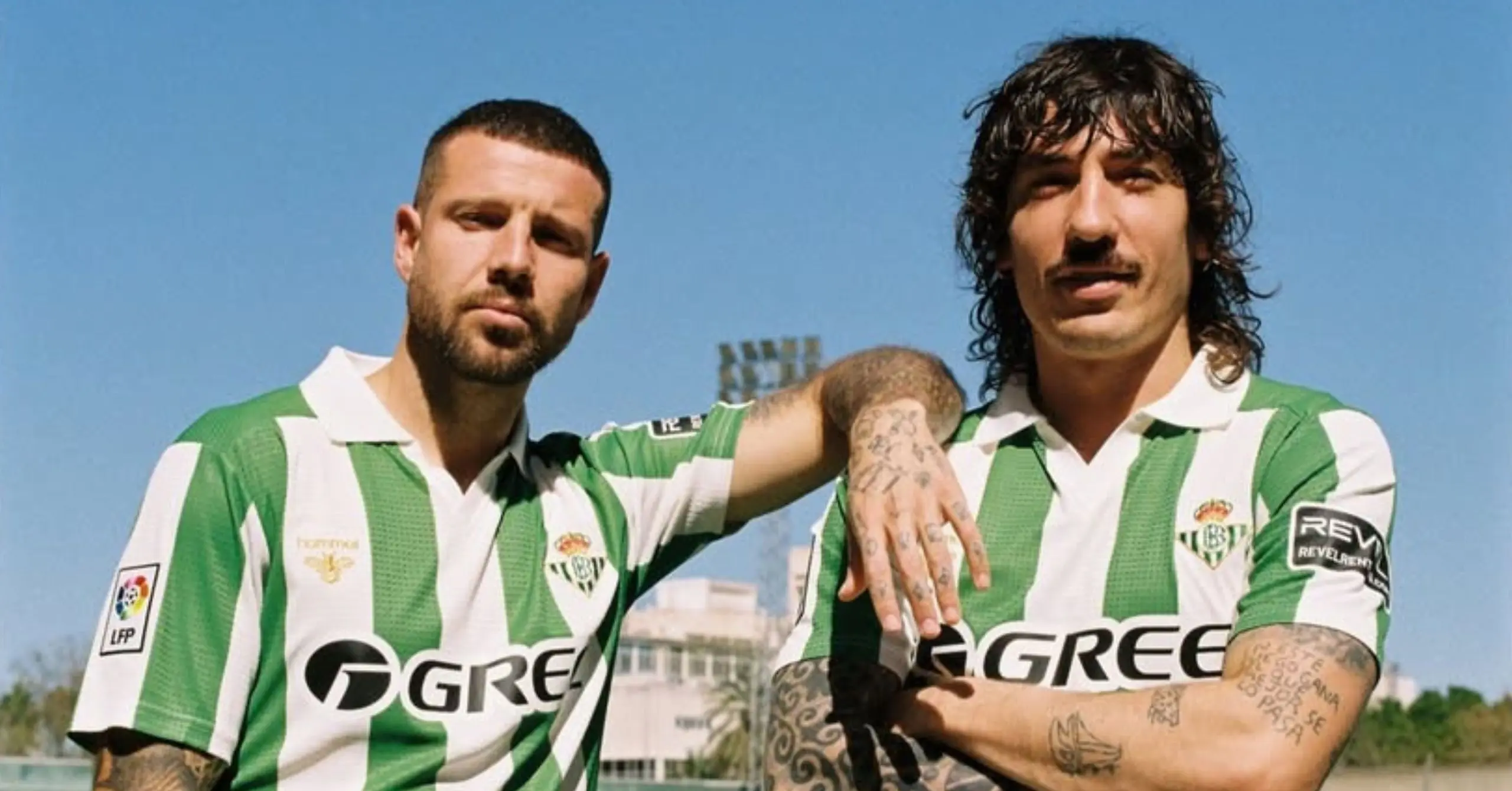 Two male soccer players in green-and-white striped jerseys pose with arms around each other on a sunny day.