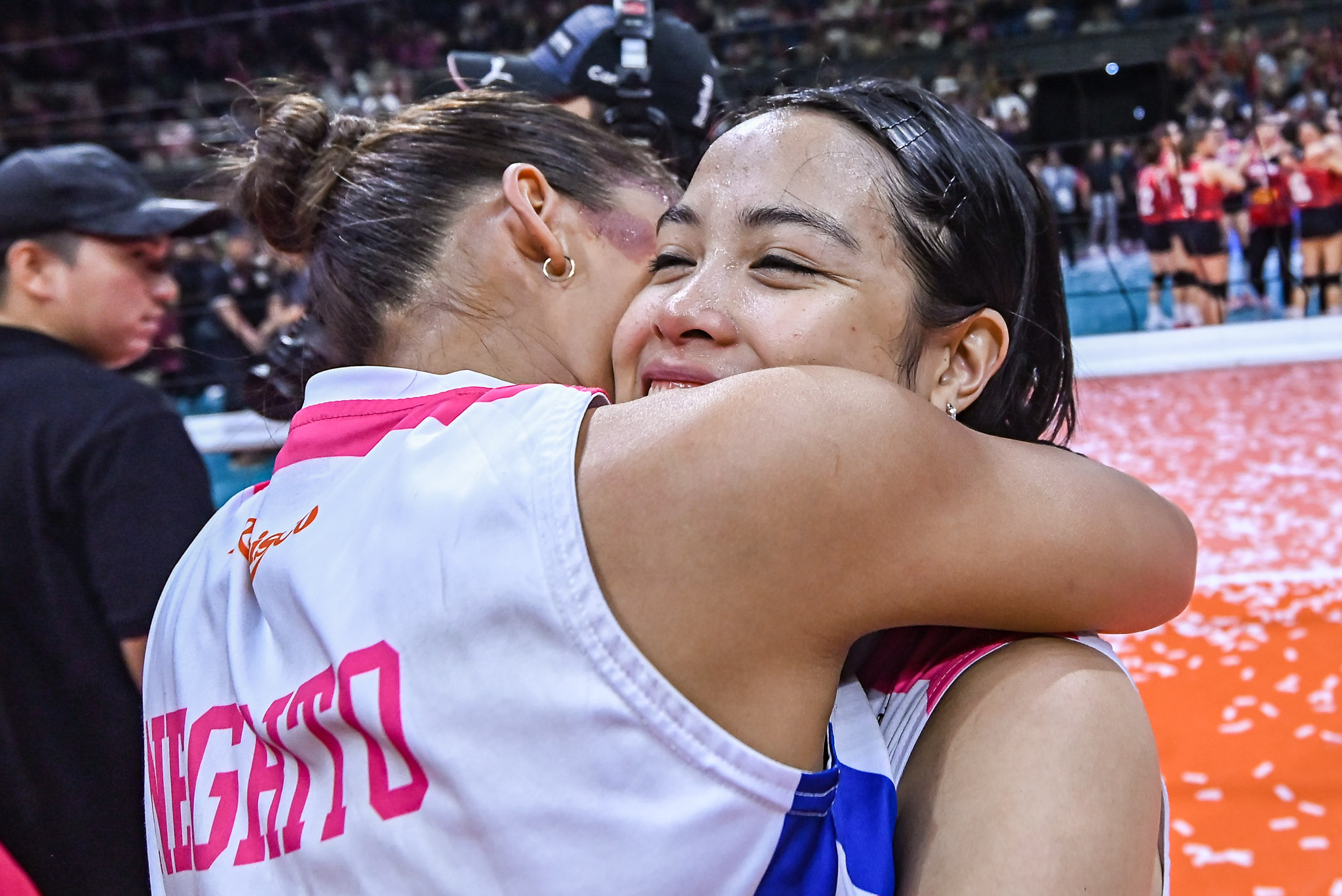 Jema - the game Two athletes embrace in a stadium, one smiling with eyes closed as the crowd cheers behind them.