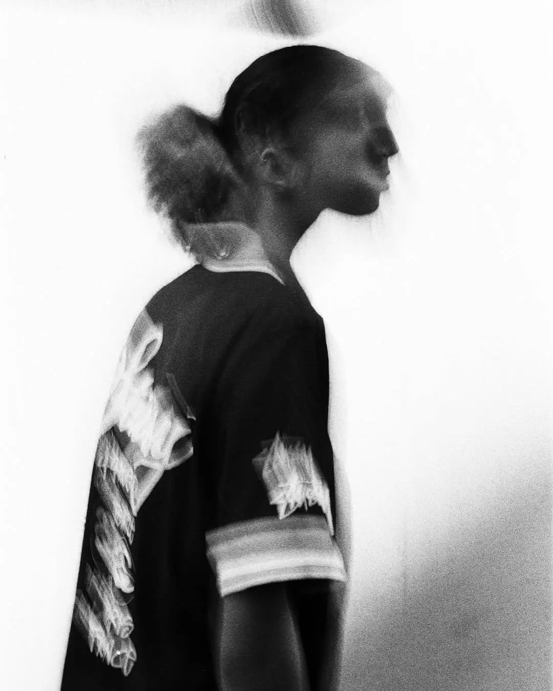 Black-and-white double-exposure portrait in profile, a person wearing a dark graphic tee against a light background.