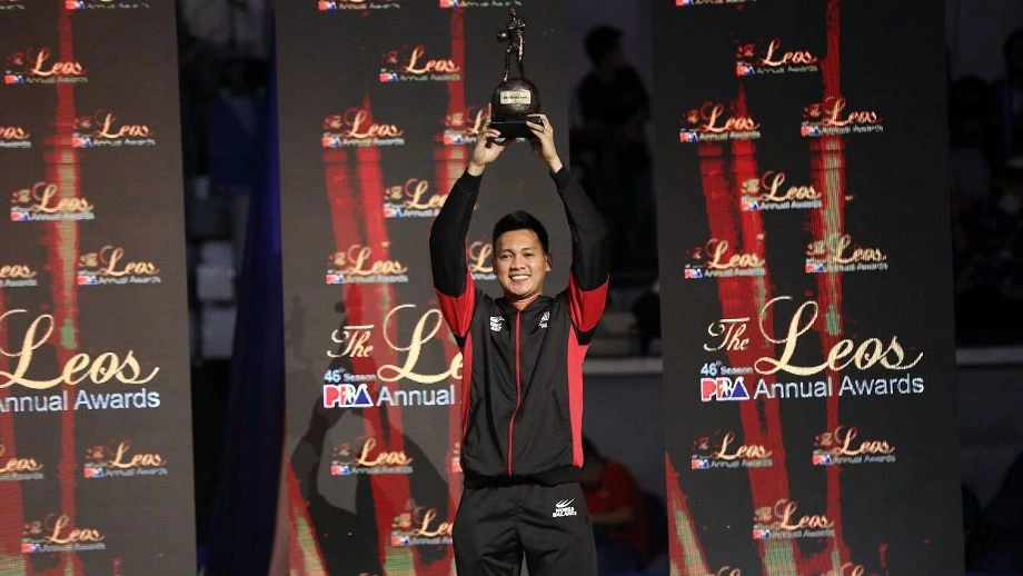 Man on stage lifts a trophy above his head during an awards ceremony with a dark backdrop reading 'Leos Annual Awards'.
