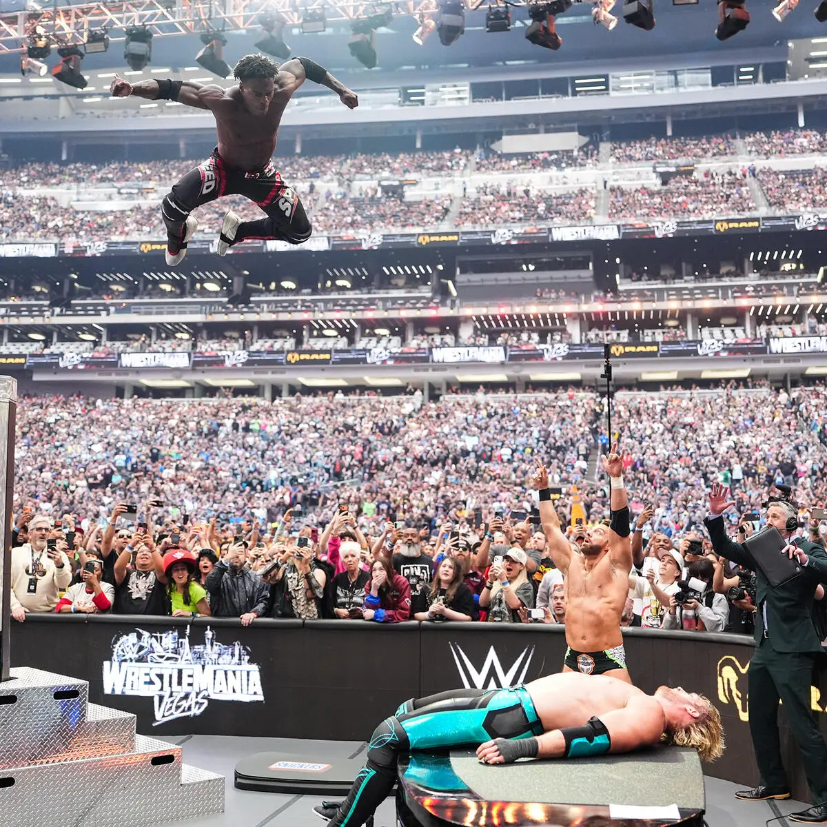 Wrestler leaps from the top-left toward the crowd during WrestleMania Vegas as fans cheer in a packed stadium.