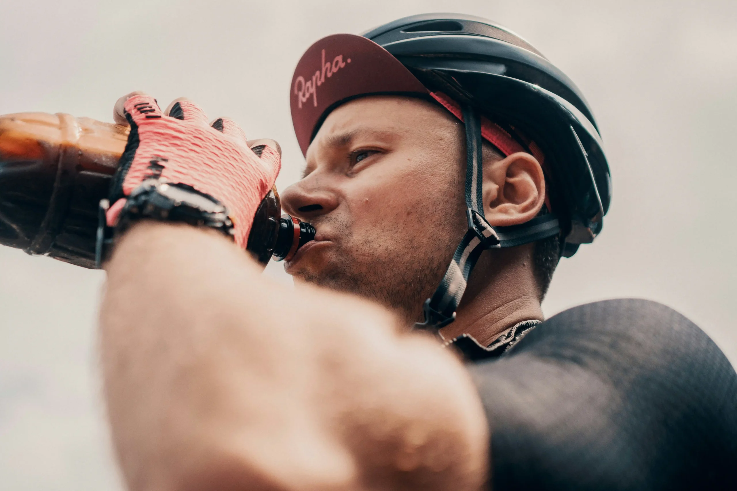 Viktor-bystrov-mn7etqfhnhc-unsplash - the game Cyclist in a helmet drinks from a water bottle held up to his mouth.
