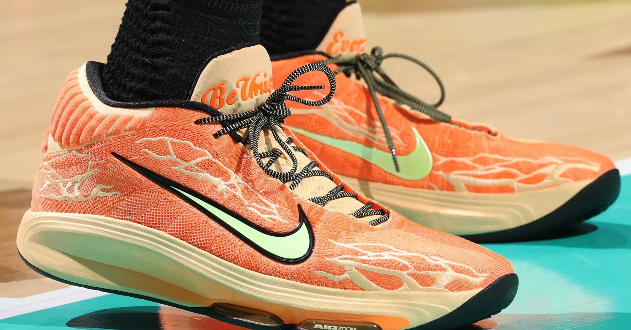 Close-up of orange running shoes with a mint-green Nike swoosh and black-and-white laces on a turquoise surface.