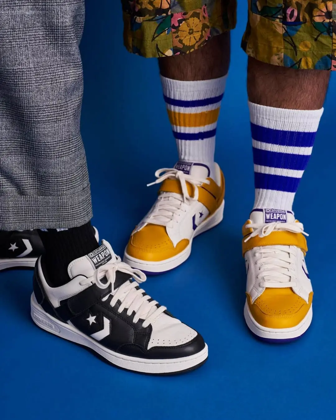 Two sneakers on a blue background: a black-and-white shoe on the left and a yellow-and-white shoe on the right, paired with striped socks and colorful shorts.