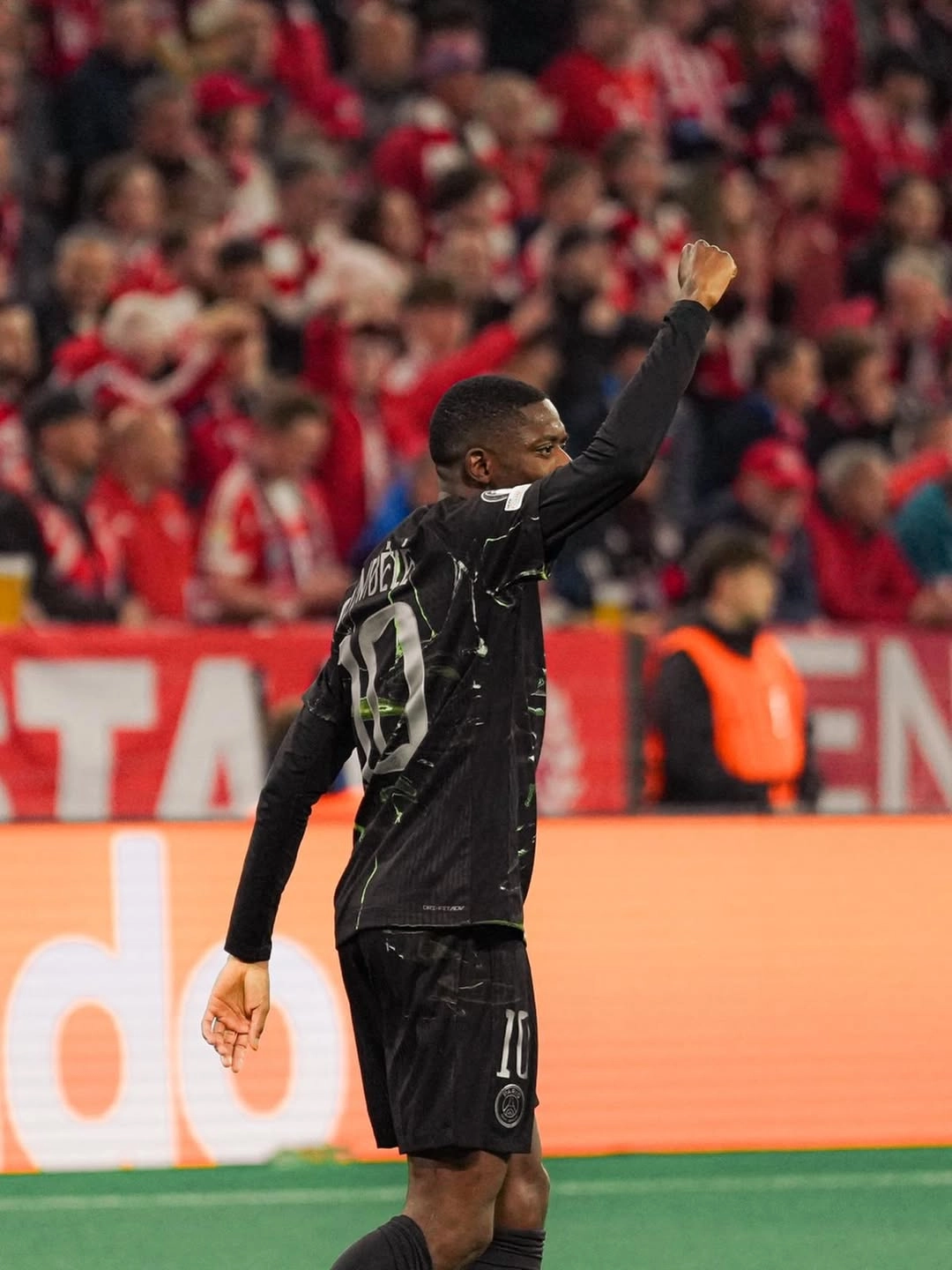 Dembele - the game Soccer player in black kit raising a clenched fist as fans cheer in the background.