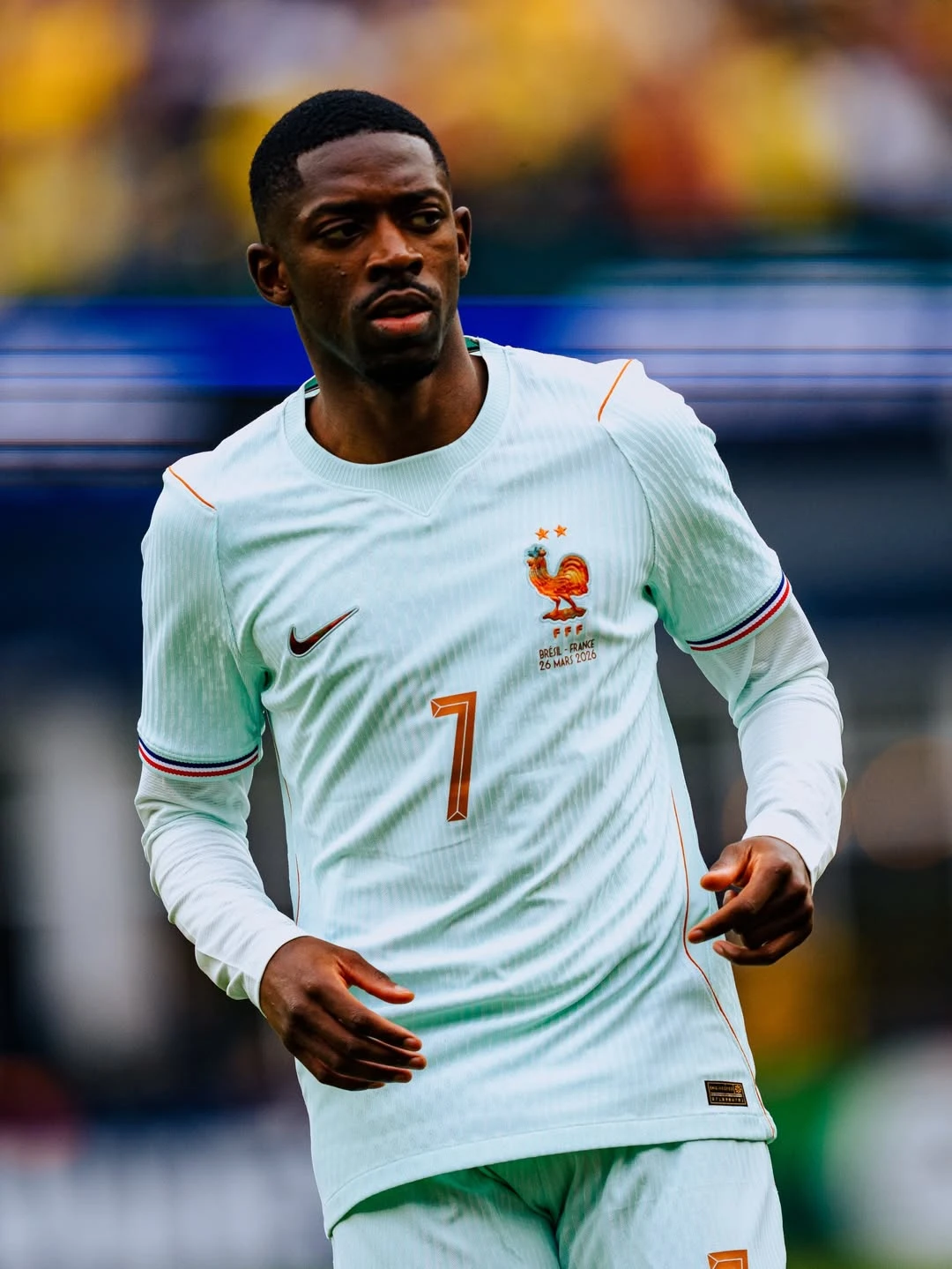 France away - the game French national team footballer in a light blue away kit with the rooster emblem, number 7, running on the pitch during a match with blurred stadium background.