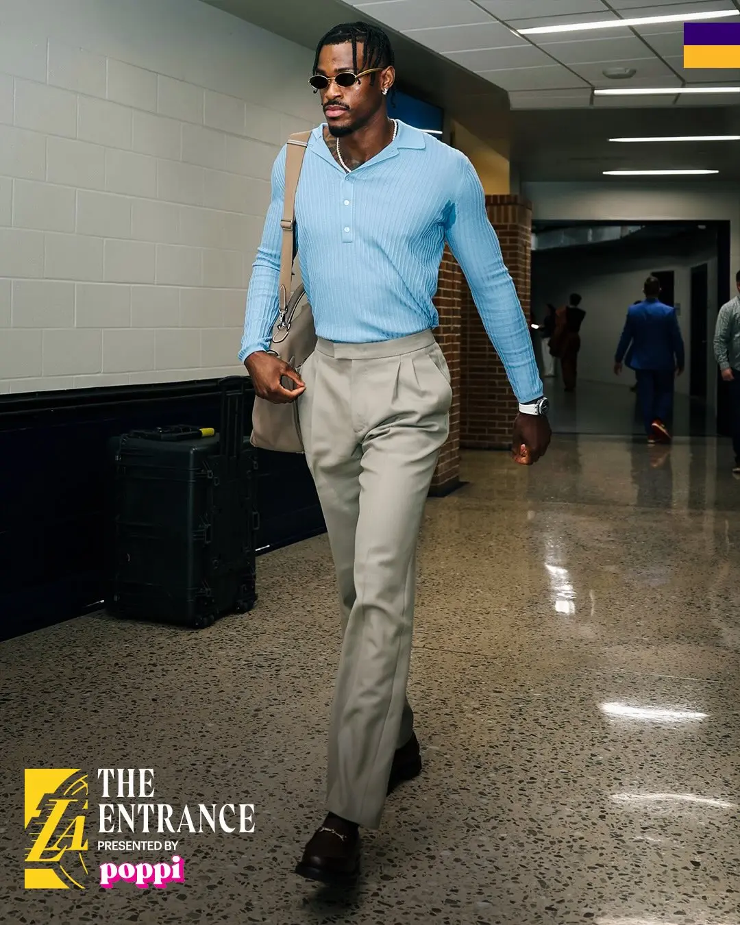 Jarred vanderbilt - the game Stylish man in a light blue polo, beige dress pants, sunglasses, and a beige shoulder bag walking down a hallway; event watermark in corner.