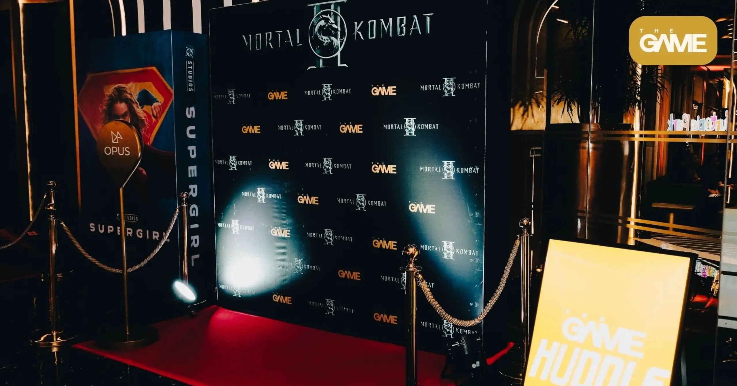 Red carpet event area with a black backdrop displaying Mortal Kombat and The Game logos, roped-off entry.