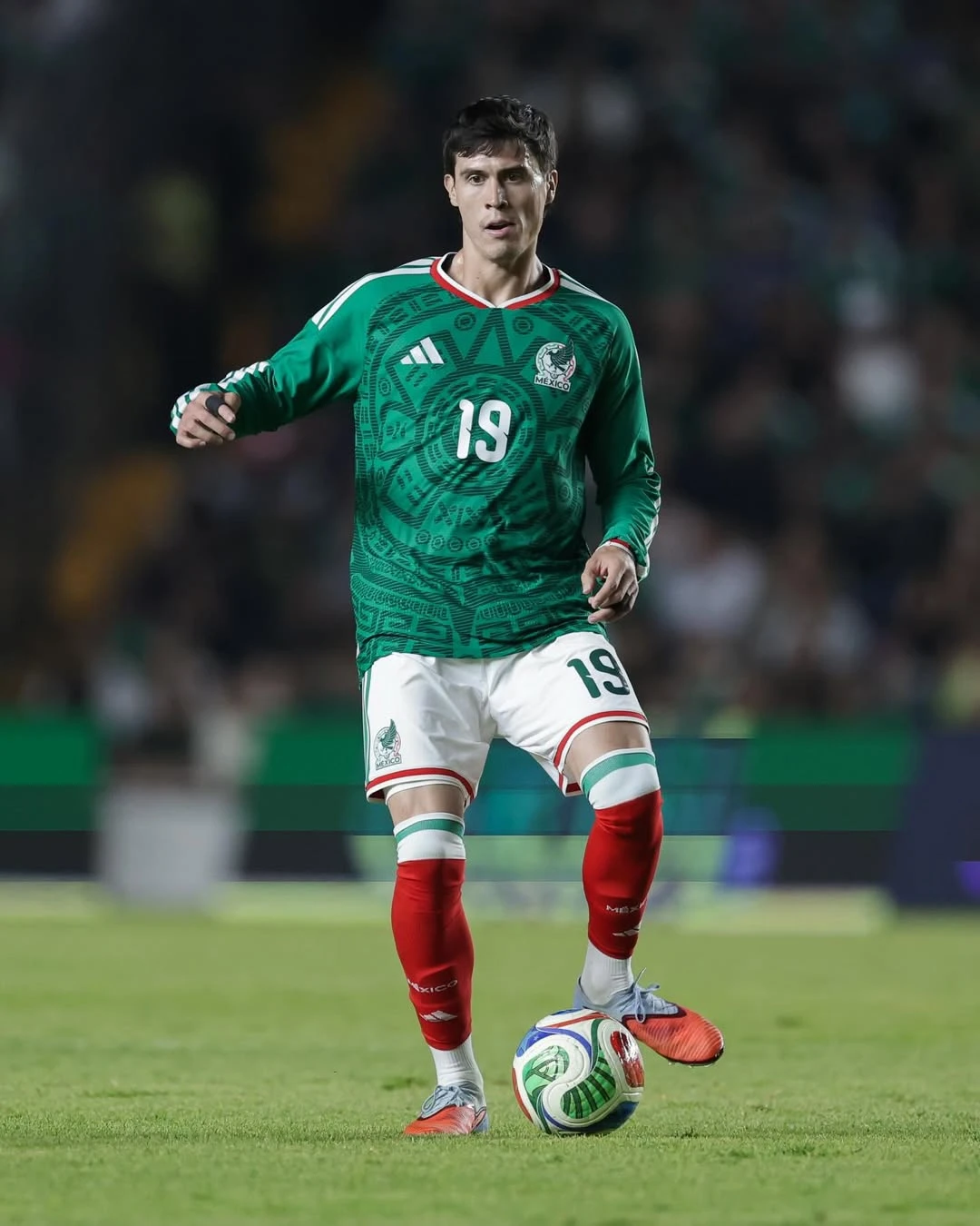 Mexico home - the game Mexican soccer player in a green jersey with number 19 dribbling a ball on the field.