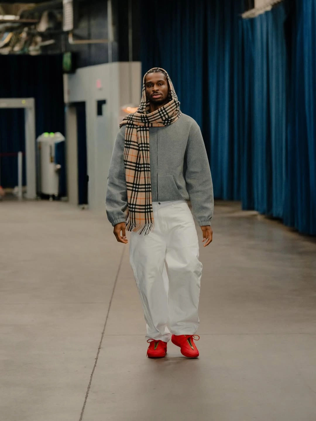 Sga burberry - the game Professional basketball player Shai Gilgeous-Alexander walks down an arena tunnel wearing a bold winter look. He pairs a minimalist grey zip-up hoodie with ultra-baggy white cargo trousers. The outfit is styled with a classic Burberry check cashmere scarf draped over his head and shoulders. He anchors the look with vibrant, bright red low-top sneakers.
