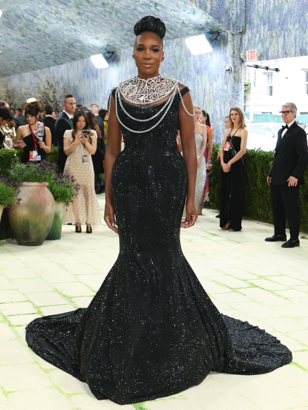 Snapinstato_684949929_18579765421050757_8366413845072198711_n - the game Woman in a floor-length black glitter gown with a silver ornate neckpiece and draped chain jewelry, posing on a light-tiled walkway at an event.