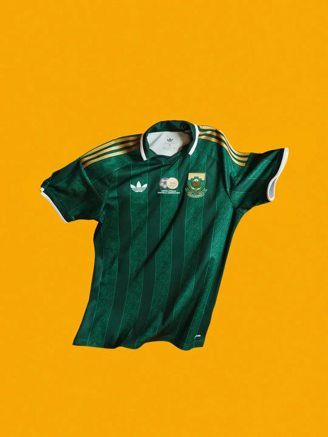 South africa away - the game Green striped athletic jersey with white collar and gold shoulder stripes, displayed on a bright orange background, featuring team crest on chest.