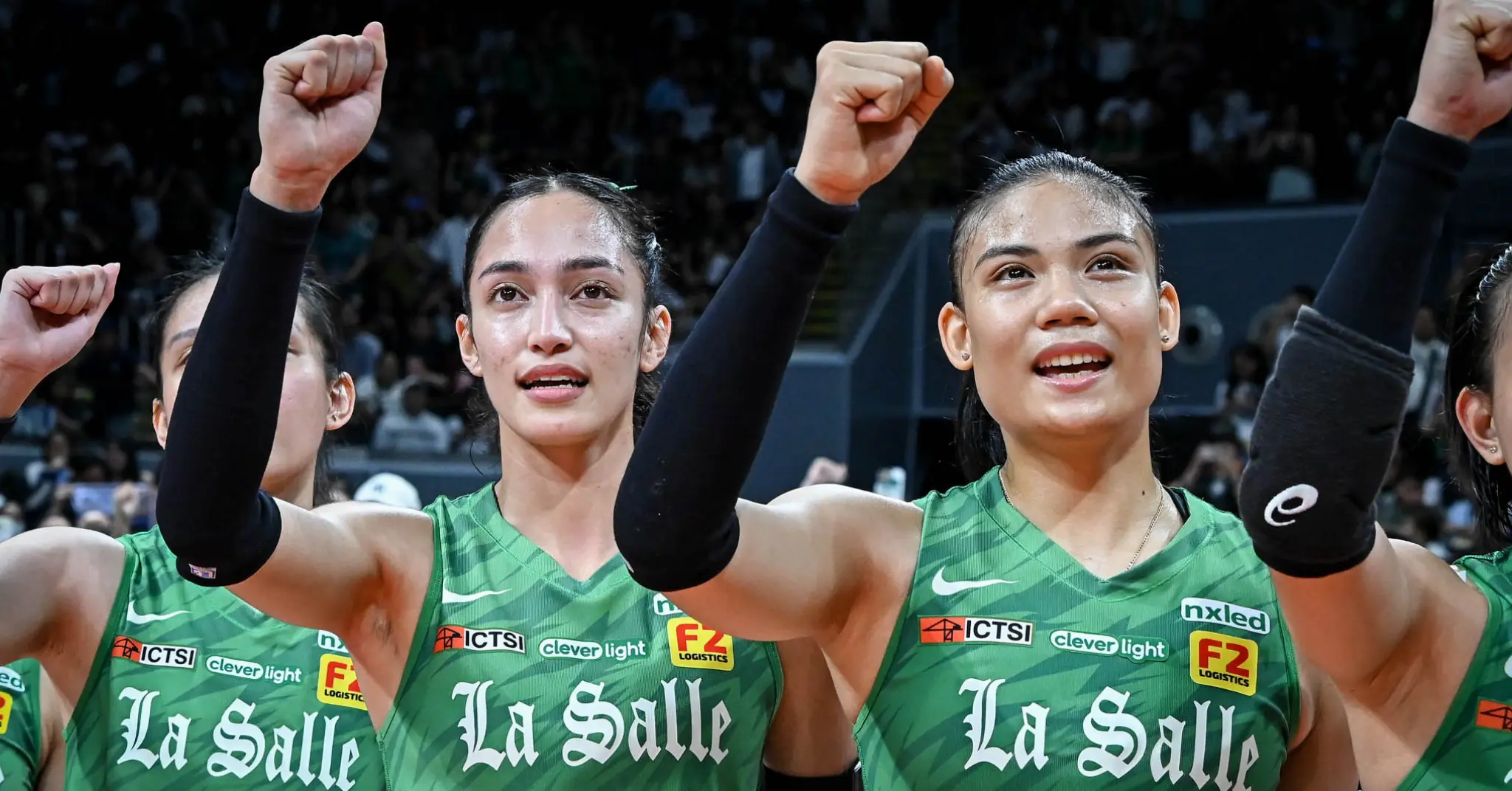 Three female athletes in green La Salle jerseys raise their fists in celebration on the court after a win.