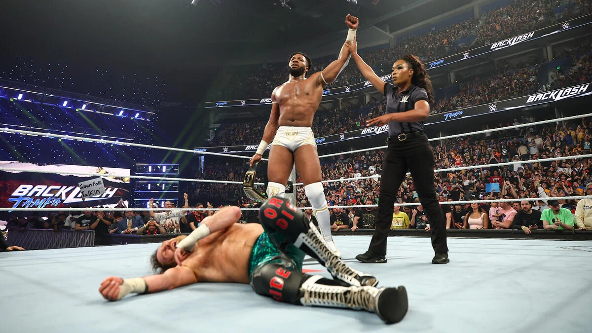 Trick - the game WWE wrestler in white trunks raises his arm with the referee as the crowd cheers, belt in hand; a defeated opponent lies on the ring mat.