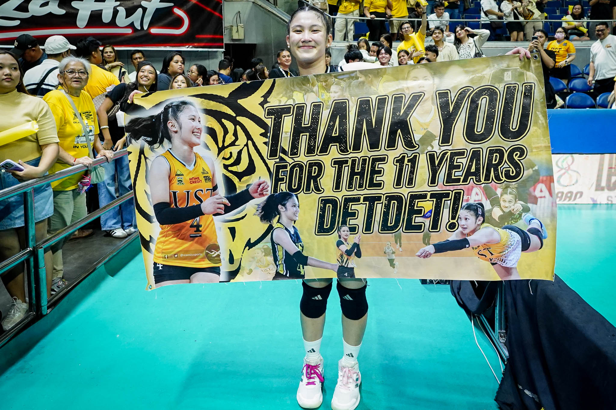 Uaap 88 wvb f4 ust vs nu- det pepito-01290 - the game Volleyball player holding a large banner that reads 'THANK YOU FOR THE 11 YEARS' at an indoor arena, with cheering fans in yellow in the background.