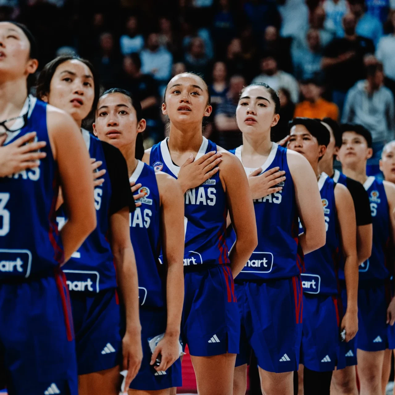 Group of female basketball players in blue uniforms standing with hands over their hearts during the national anthem.