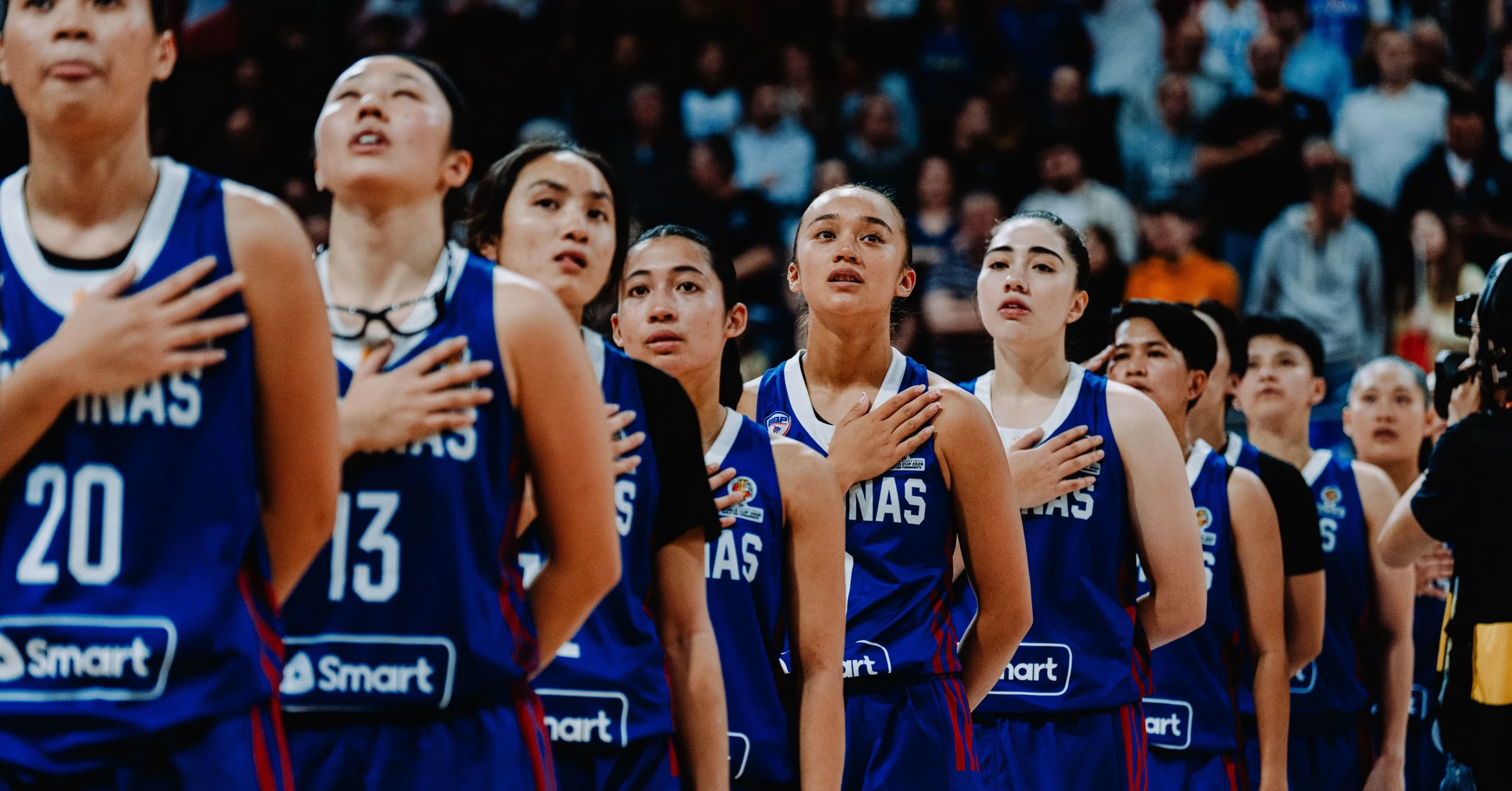 Group of female basketball players in blue uniforms standing with hands over their hearts during the national anthem.