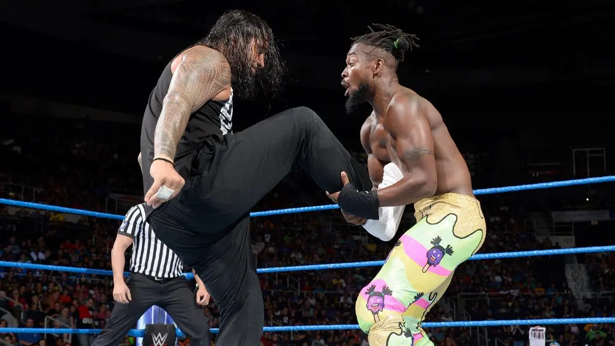 Two wrestlers collide in the ring as one delivers a high kick to the other's chest beside the referee.