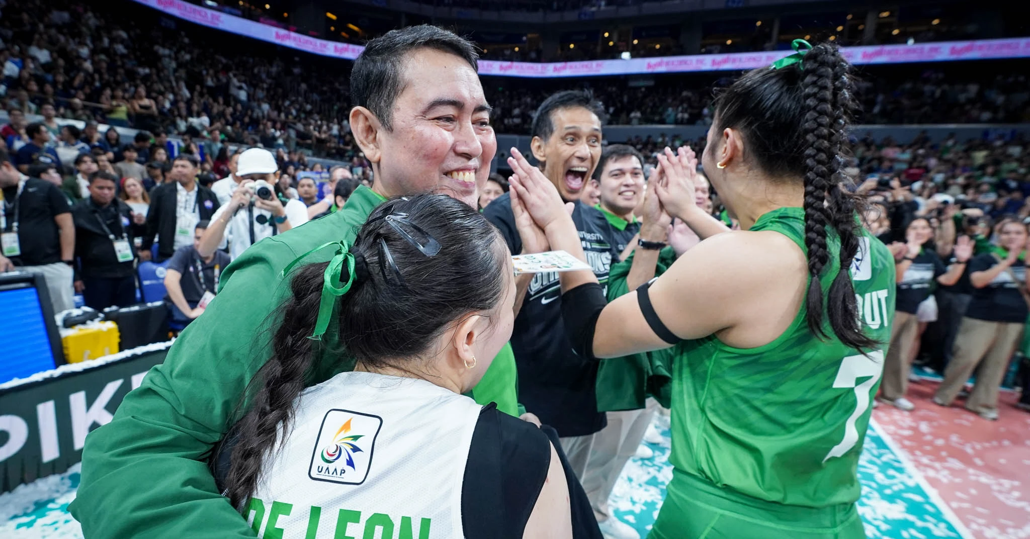 Group of athletes in green uniforms celebrate with hugs in a crowded indoor arena.