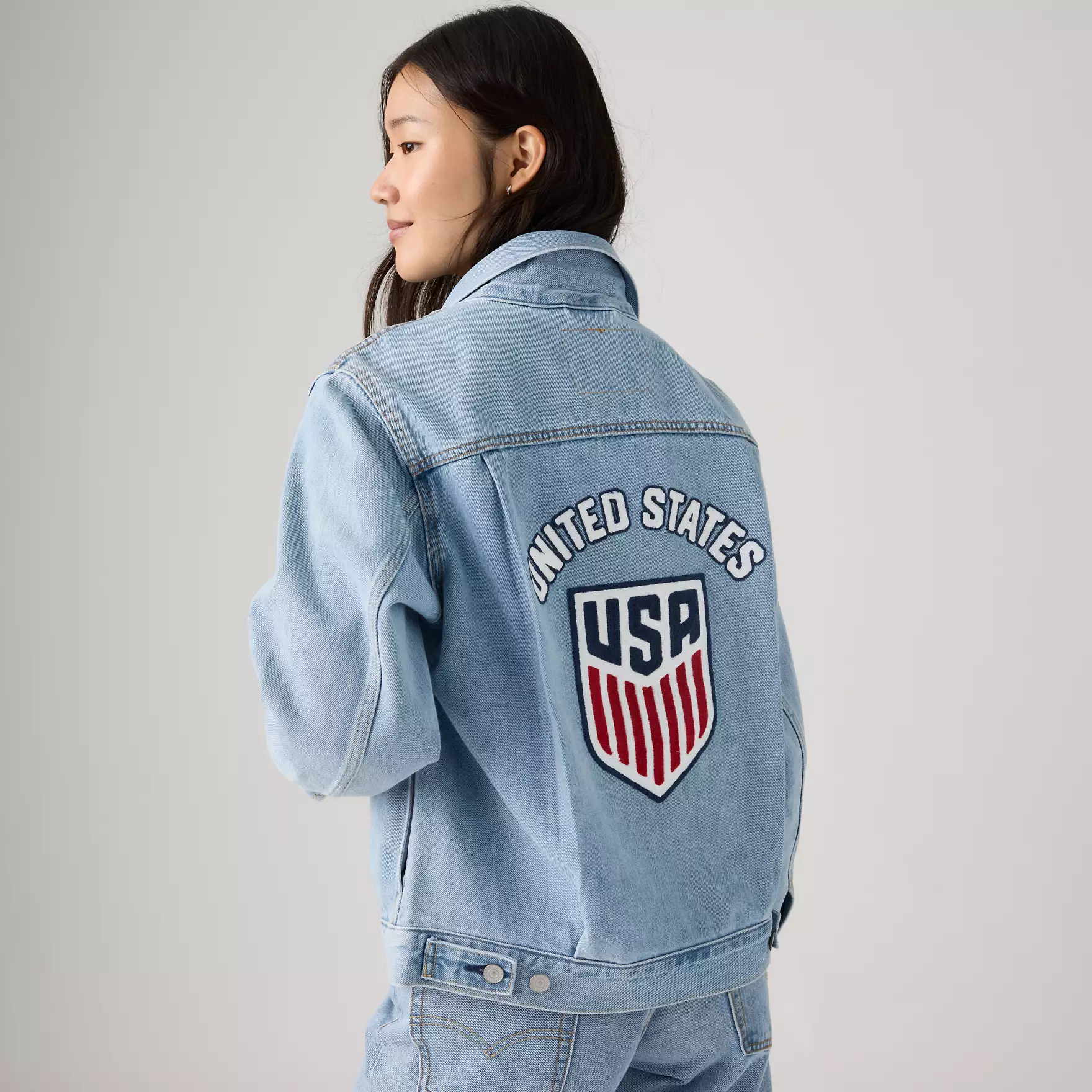 Side profile of a person wearing a light blue denim jacket with a large United States patch on the back.